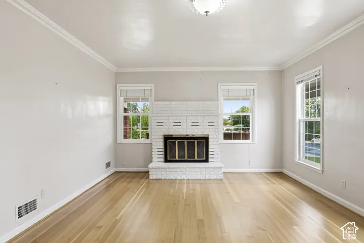 Painted brick fireplace with a metal surround, wood-finish flooring, crown molding, and double-hung windows