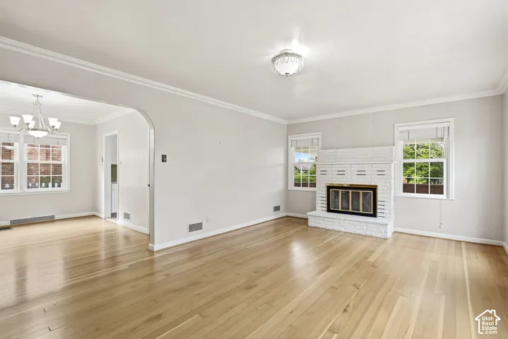 Living area featuring wood-finish flooring, white painted brick fireplace with a metallic insert, arched architectural detailing, crown molding, and dual-light fixtures