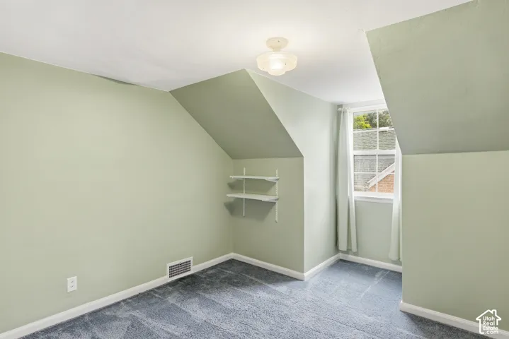 Interior room featuring sloped ceilings, wall-to-wall carpeting, a double-hung window, white built-in shelving, and an overhead glass light fixture