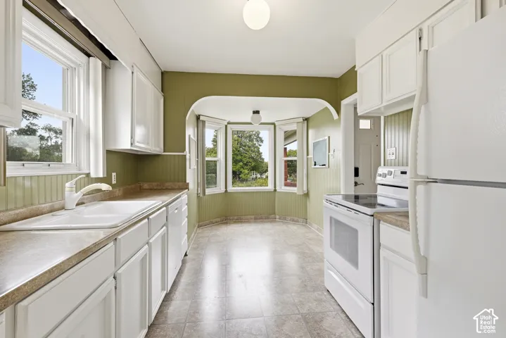 Kitchen featuring white cabinetry, solid-surface countertops, beadboard wainscoting, tile flooring, and a bay window