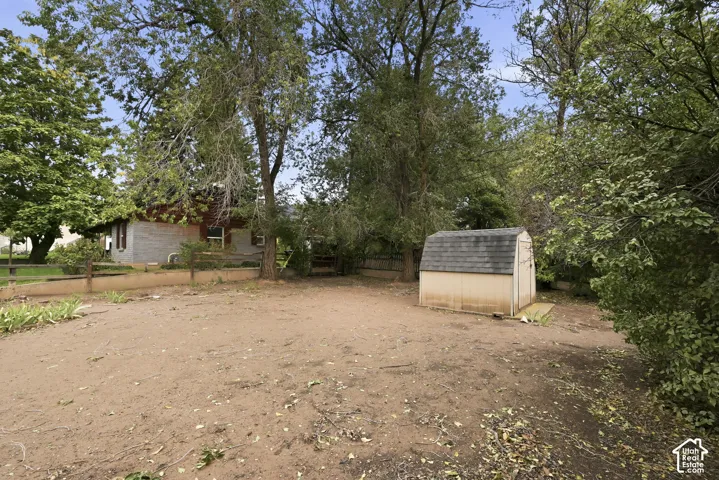 Backyard featuring mature trees, a detached storage shed, perimeter fencing, and a retaining wall
