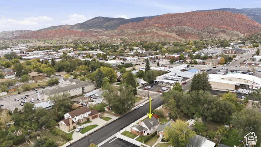 Aerial perspective featuring a detached residential property with a gabled roofline and an attached carport, set against a backdrop of prominent mountain ranges