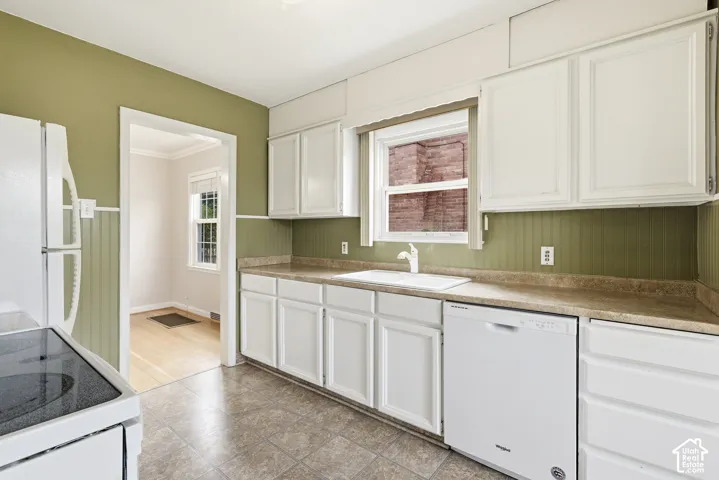 Kitchen featuring white shaker-style cabinetry, beadboard wall paneling, solid-surface countertops, integrated dual-basin sink, and tile flooring