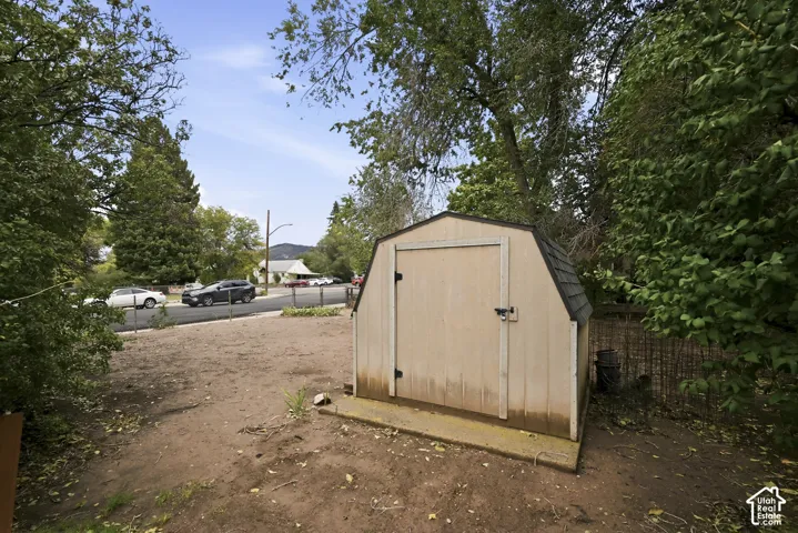 Exterior storage structure with a gambrel roof and concrete foundation pad, situated within a partially fenced lot with mature trees