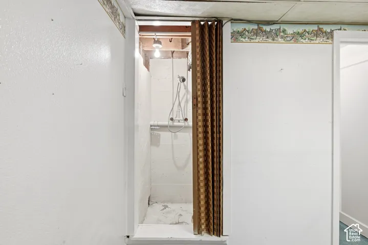 Shower stall featuring a wall-mounted showerhead, exposed ceiling joists, and a folding privacy screen