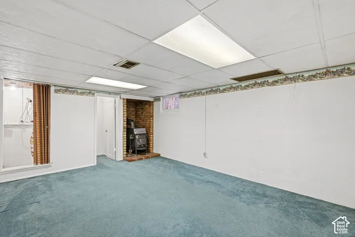 Finished room featuring a drop ceiling, inset brick fireplace, wall-to-wall carpeting, and a built-in shower stall