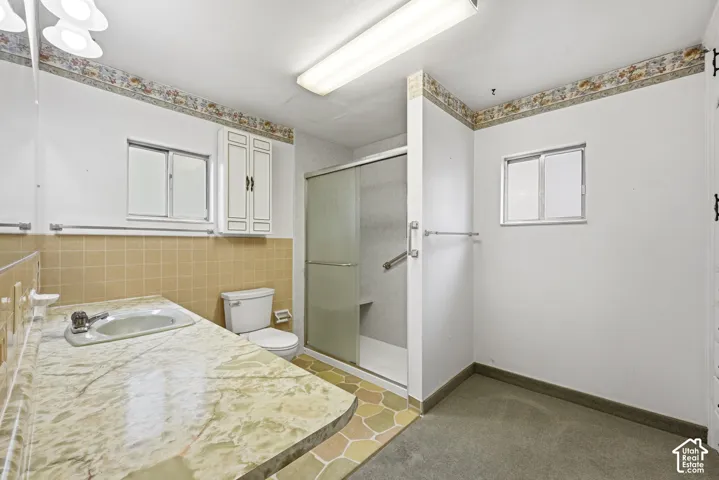 Bathroom featuring a vanity with a patterned countertop and integrated sink, a glass-enclosed shower stall, built-in cabinetry, and tile flooring