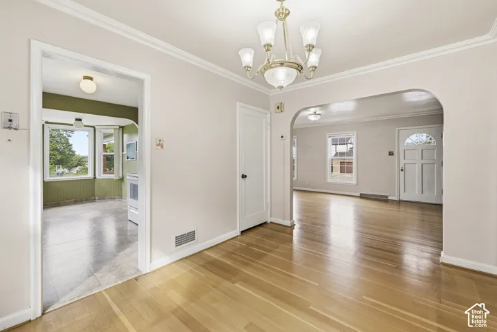 Interior space featuring hardwood flooring, arched thresholds, crown molding, and a multi-arm brass chandelier