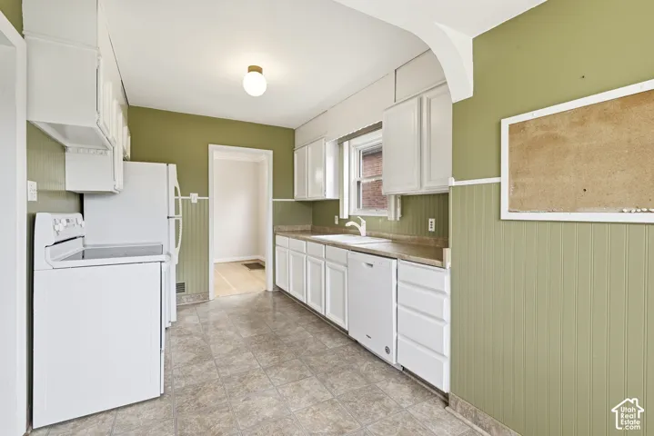 Kitchen featuring white cabinetry, solid-surface countertops, beadboard wainscoting, a double-basin sink, and tile flooring