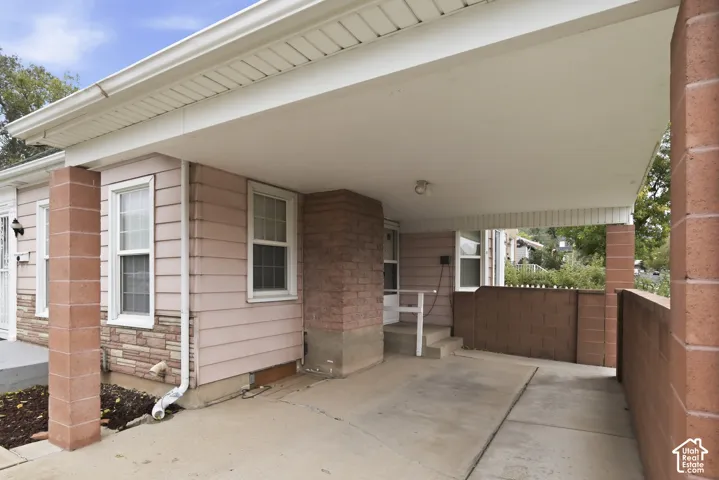 Covered carport featuring masonry support pillars, concrete flooring, stone-veneer siding, and an attached privacy wall