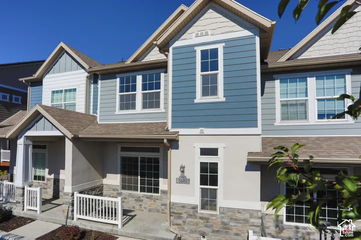 Multi-level exterior featuring a stone veneer facade, horizontal lap siding, shingle-style gable accents, a covered front porch with white railing, and multi-pane windows