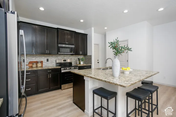 Kitchen featuring dark cabinetry, stone-surface countertops, a center island with sink, mosaic-tile backsplash, and recessed lighting