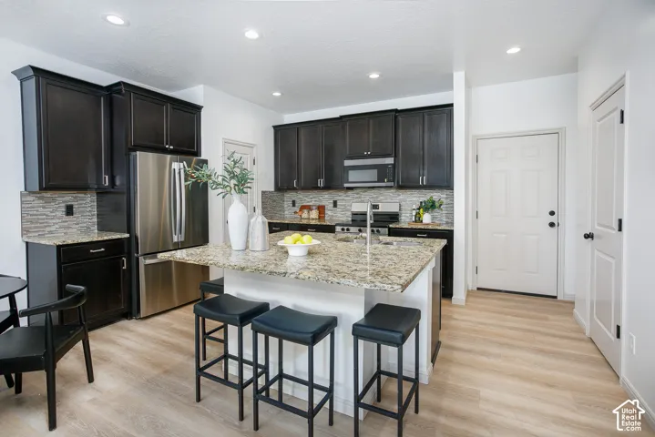 Kitchen featuring dark wood cabinetry, stone countertops, central island with integrated sink, stainless steel appliances, and wood-finish flooring