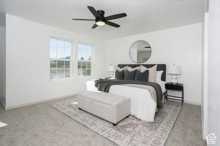 Neutral-toned interior featuring wall-to-wall carpeting, dual windows, and a matte black ceiling fan with integrated lighting