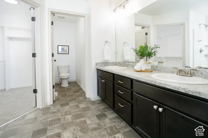 Dual-sink vanity with stone-finish countertop, dark cabinetry, full-width wall mirror, and tile flooring
