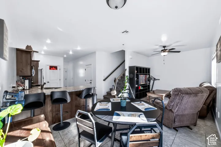 Open concept interior featuring stone-finish countertops, dark wood-tone cabinetry, tiled flooring, and a staircase with a wooden handrail