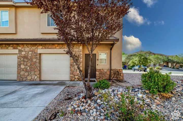 Exterior facade featuring stucco siding, stone veneer accents, multi-pane windows, a dark-toned entry door, and an integrated garage