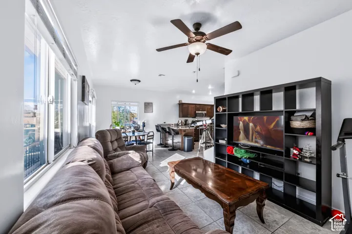 Open-concept space featuring tile flooring, a multi-blade ceiling fan with integrated lighting, and large windows