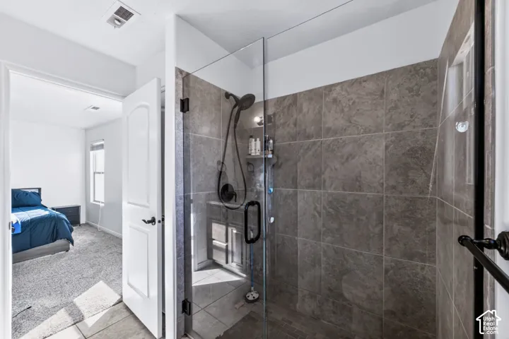 Walk-in shower featuring large-format textured tile surround, glass enclosure, and matte black plumbing fixtures