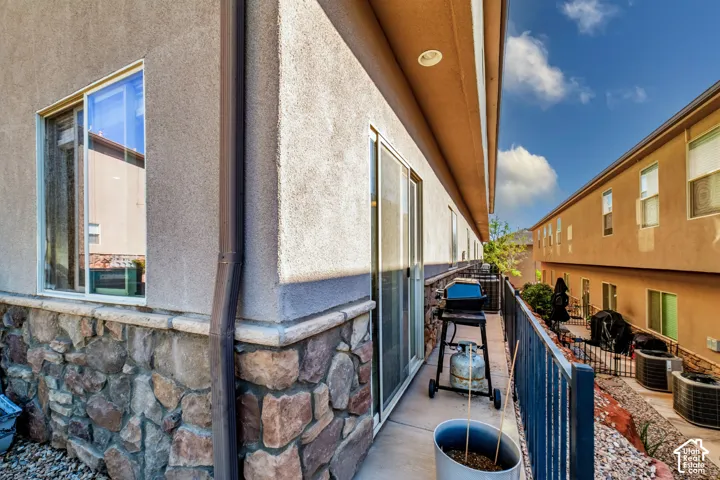 Stucco exterior finish with stone veneer wainscoting, sliding glass door, metal balcony railing, and recessed exterior lighting
