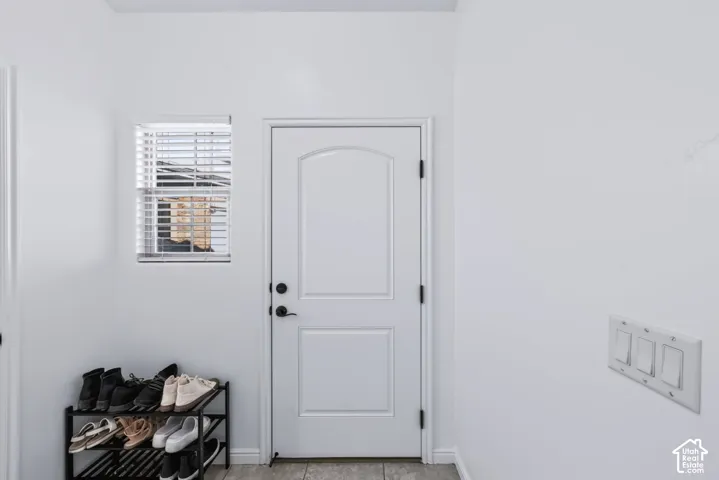 Entryway featuring a white paneled door with matte black hardware, a window with horizontal blinds, and tile flooring