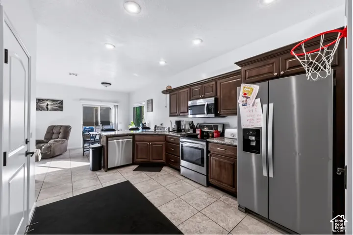 Kitchen featuring dark wood cabinetry, stone-surface countertops, stainless steel appliances, tile flooring, and recessed lighting