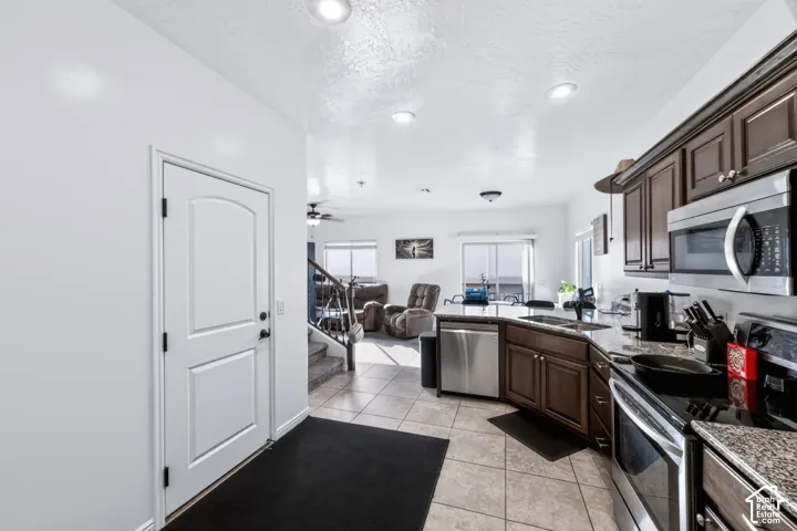 Kitchen featuring dark wood cabinetry, stainless steel appliances, stone-look countertops, and tile flooring