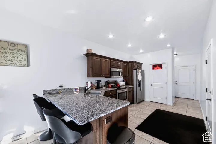 Kitchen featuring dark wood cabinetry, stone-finish countertops, tile flooring, and recessed ceiling lighting