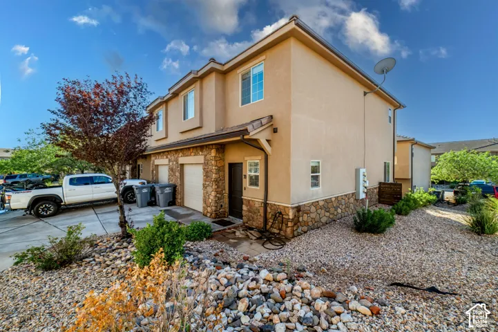 Two-story end unit townhome featuring stucco siding, stone veneer accents, an attached garage, and xeriscaped ground cover