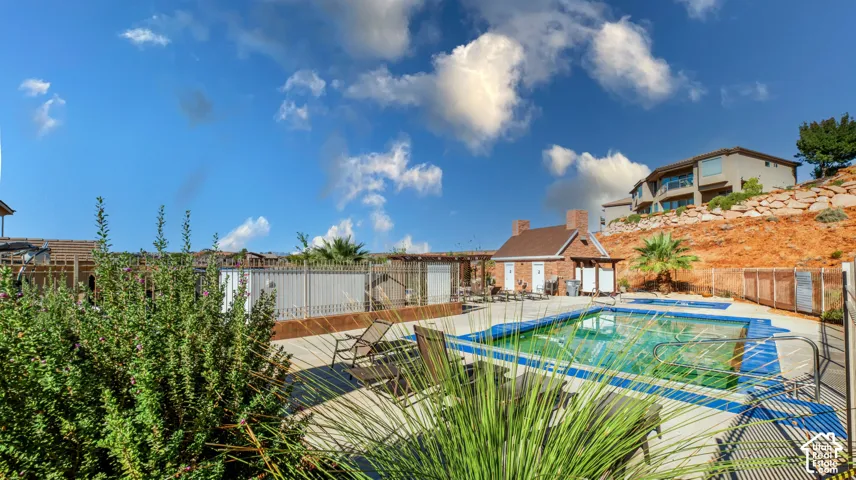 Swimming pool featuring a concrete deck, red brick pool house, metal perimeter fencing, and terraced rock landscaping