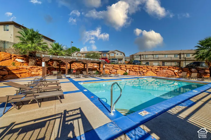 Swimming pool with blue concrete decking and a wood-frame pergola set against a natural red rock landscape