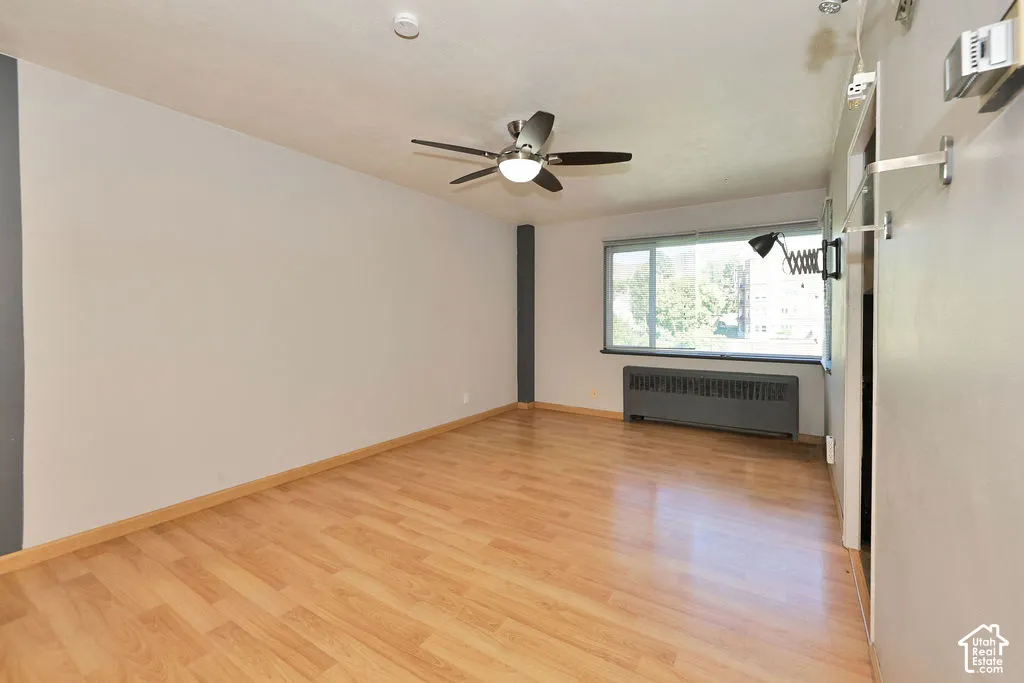 Interior room featuring light-toned wood-finish flooring, a ceiling-mounted light fixture with a fan, and a large horizontal window