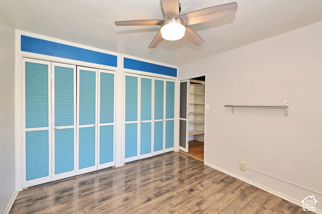 Wood-finish flooring, dual bi-fold closet systems with louvered panels, integrated built-in shelving, and a brushed nickel ceiling fan with central lighting