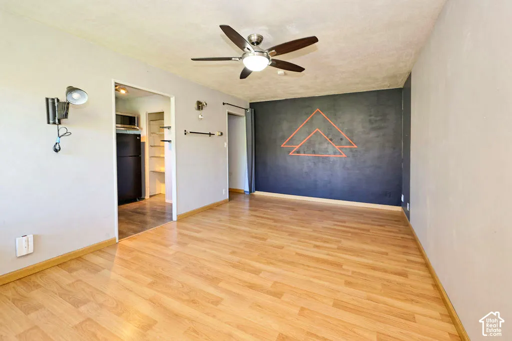 Interior space featuring wood-finish flooring, a dark accent wall, a central ceiling fan with integrated lighting, and wall-mounted metal light fixtures