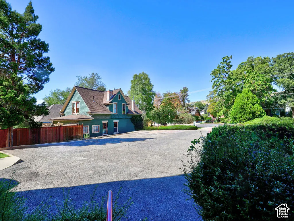 Two-story structure with green siding, asphalt shingle roof, paved surface area, wooden privacy fencing, and mature trees