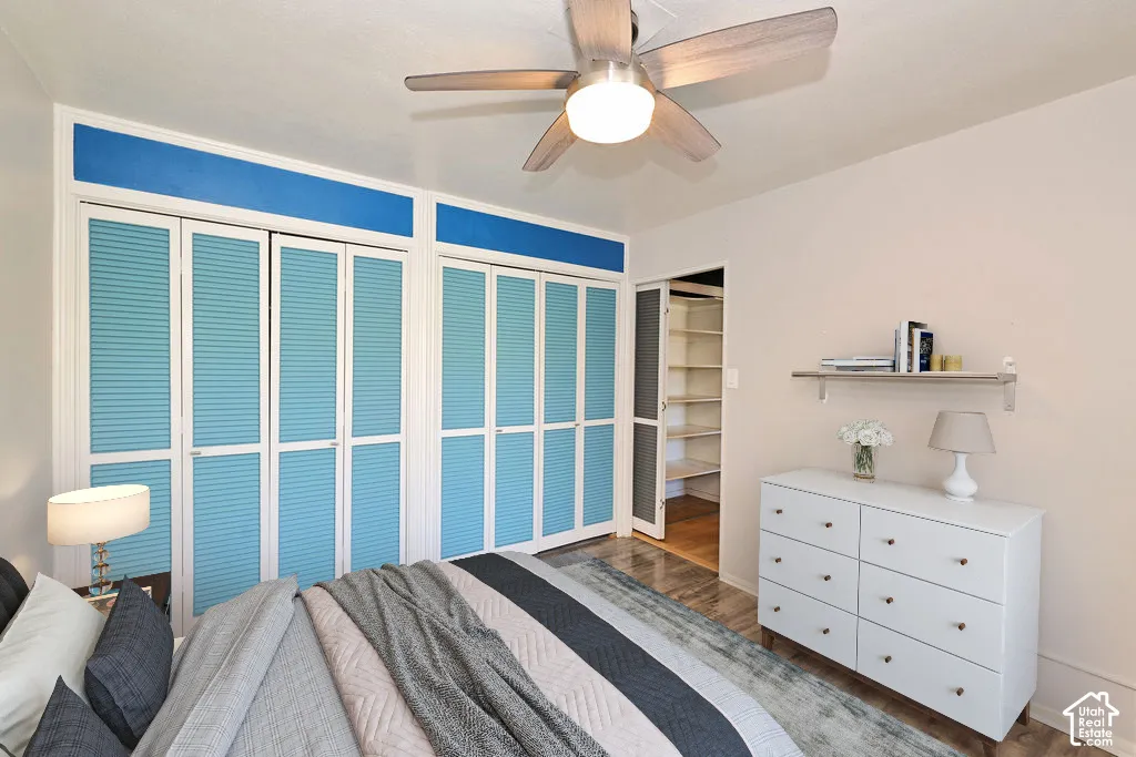 Dual floor-to-ceiling louvered door closets, metal-finish ceiling fan with integrated lighting, and wall-mounted shelving unit