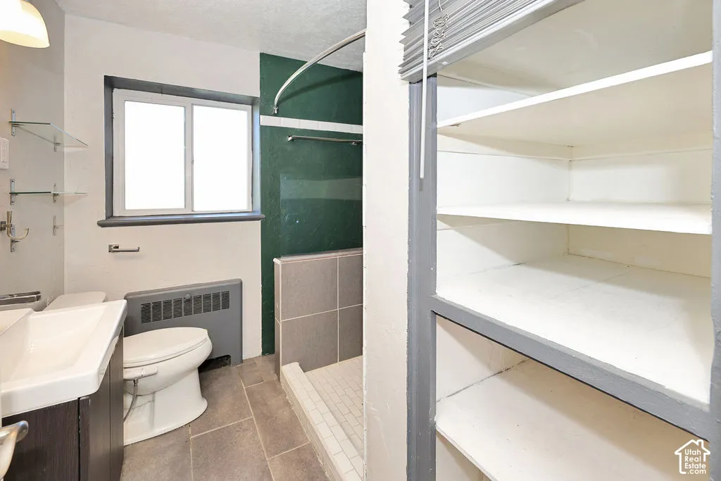 Bathroom featuring tiled flooring, a walk-in shower with tiled surround, built-in open shelving, a wall-mounted sink, and glass wall shelving
