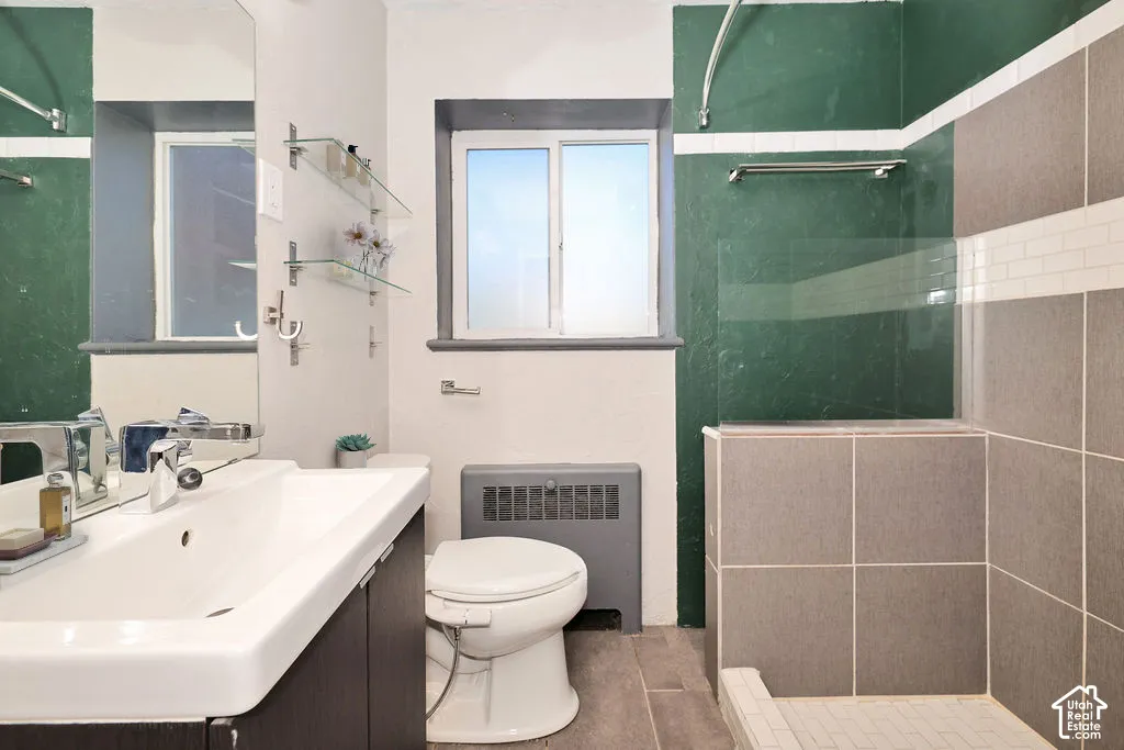 Bathroom featuring a floating vanity with a white rectangular sink, a glass shower partition, wall-mounted glass shelving, and a combination of large-format grey tile and painted green surfaces