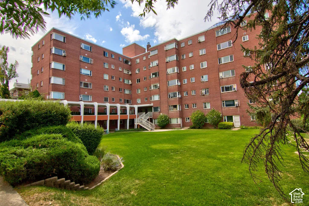 Multi-story red brick exterior featuring a covered patio, staircase access, manicured lawn, and mature landscaping