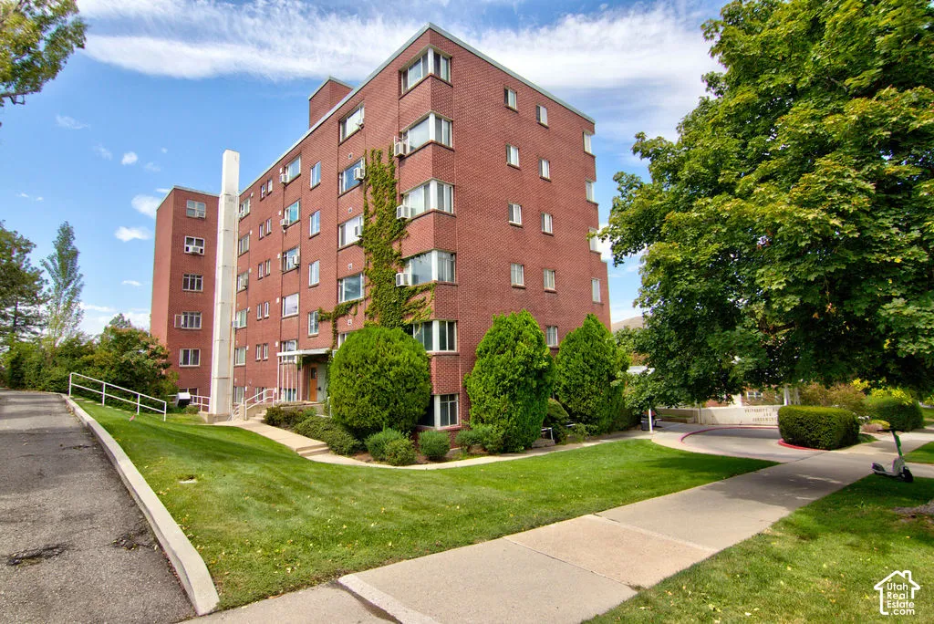 Multi-story red brick exterior featuring mature landscaping, paved pathways, and concrete stairs with metal handrails