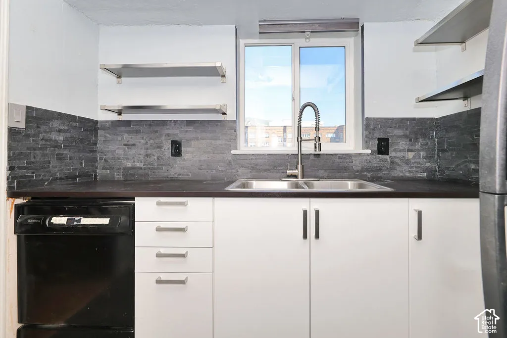 Kitchen featuring white cabinetry, dark countertops, stacked stone backsplash, stainless steel dual-basin sink with a gooseneck faucet, and open metal shelving
