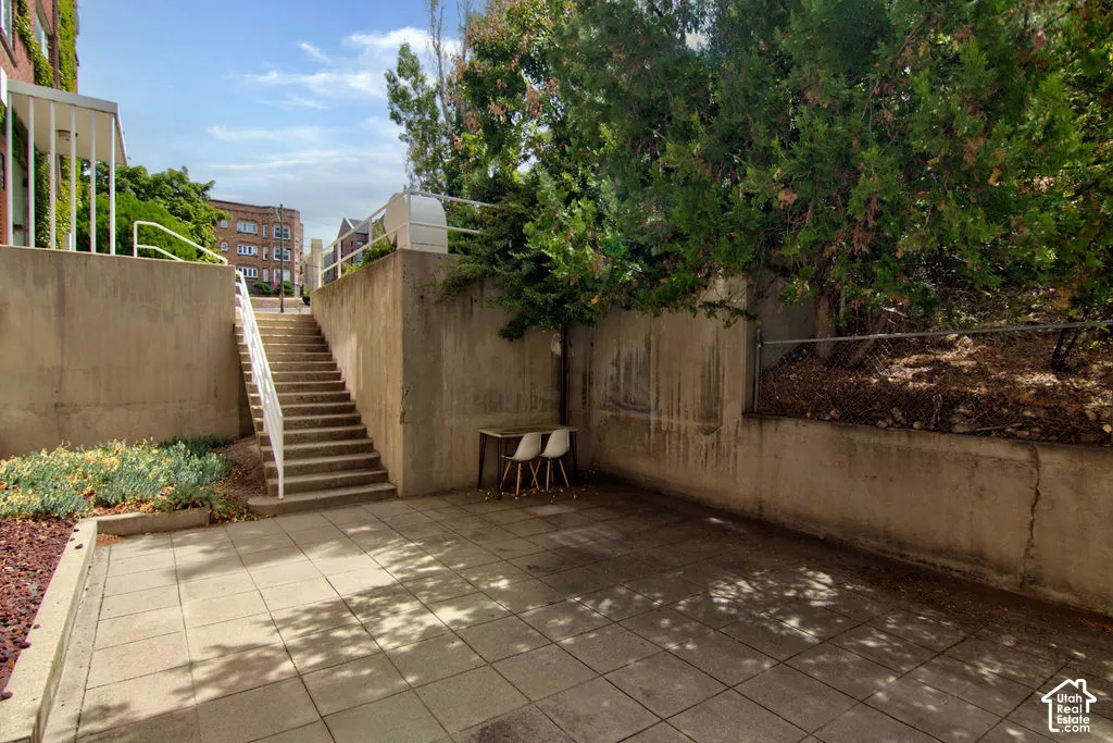 Paver patio featuring concrete retaining walls, integrated stairwell, metal railings, and mature trees