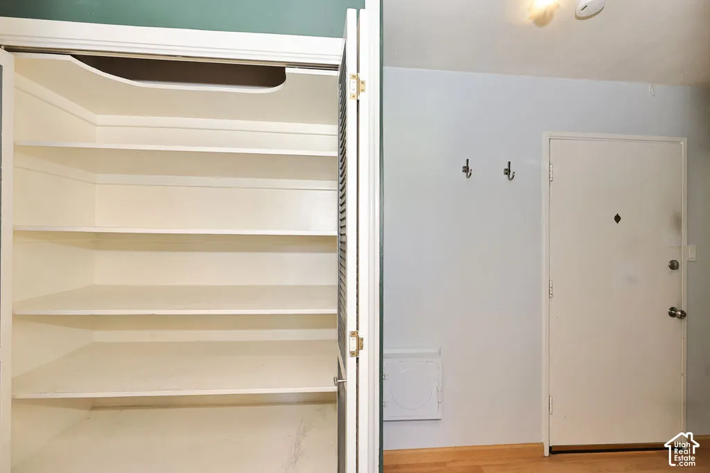 Built-in white storage shelving with louvered bi-fold doors, wall-mounted metal coat hooks, solid-core swing door with a peephole, and wood-finish flooring