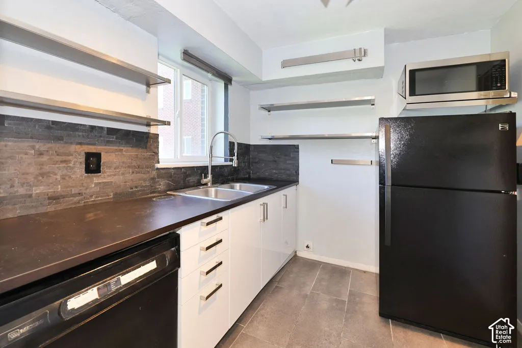Kitchen featuring white cabinetry, dark countertops, stacked stone backsplash, stainless steel floating shelving, and large-format tile flooring