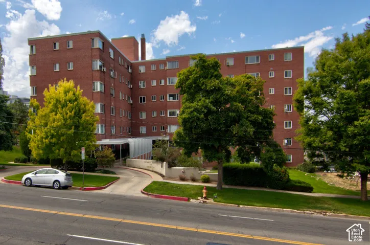 Multi-story brick exterior building featuring a covered entryway, mature trees, and landscaped grounds