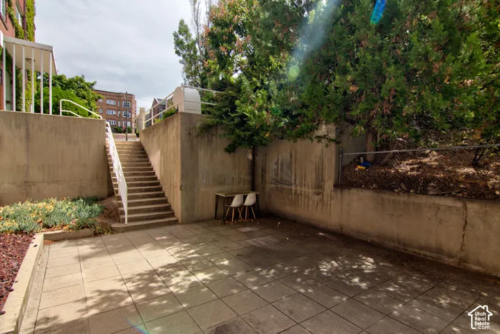Paved patio area featuring concrete retaining walls, integrated staircases with metal handrails, and mature trees