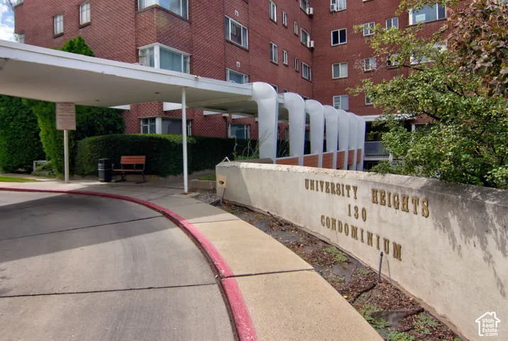 Brick facade building exterior featuring a covered entryway with structural supports, concrete circular driveway, and masonry signage