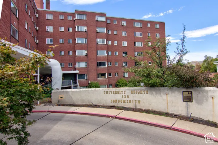 Multi-story brick condominium building featuring a curved concrete entrance drive and a masonry retaining wall