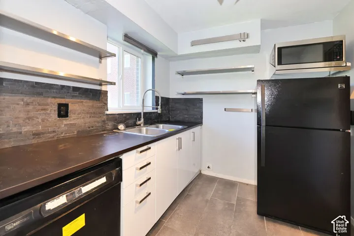Kitchen featuring white cabinetry, dark countertops, stacked-stone backsplash, stainless steel open shelving, and tile flooring