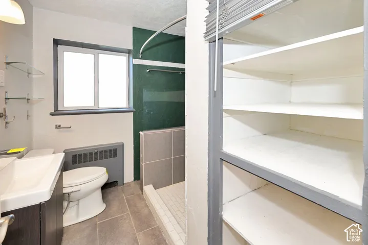 Bathroom featuring a tiled floor, walk-in shower with partial tile surround, floating vanity sink, wall-mounted glass shelving, and built-in recessed storage cabinetry